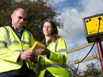 Two operatives, one female and one male, working technical equipment in the field.