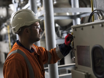 Operative wearing an orange hi vis jacket and operating technical equipment.