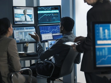 Colleagues discussing technical information on computer screens in a low lit office environment.