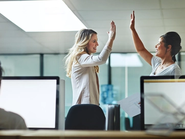 Two female colleagues performing a high five whilst smiling at each other.