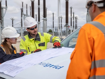 Multiple colleagues reading schematics on top of a National Grid van. They are all wearing hi vis jackets and hard hats.