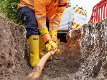 Man wearing a hi-vis digging cables under the ground.