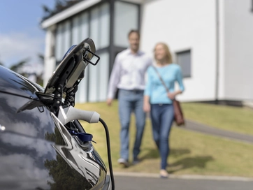 Electric vehicle charging with car owners standing in front smiling.