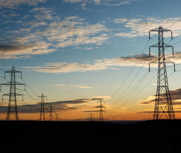 Electricity pylons positioned in a green field, with a deep orange sunset in the distance.
