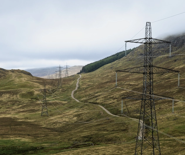Mountainous field containing multiple connected pylons. the sky is a dark grey colour indicating it will rain.